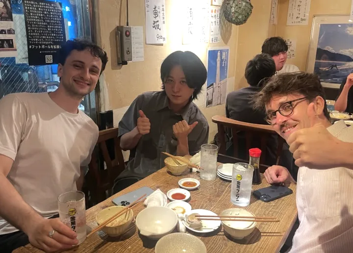 飲食店のテーブルを囲みカメラに向かってポーズをとる三人