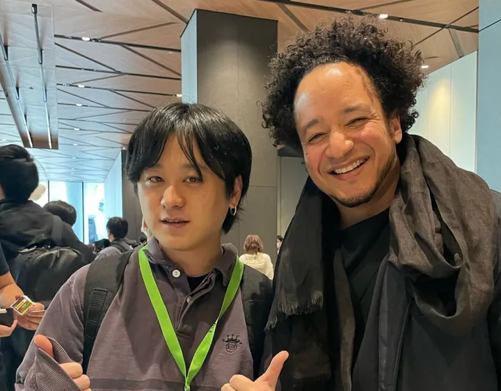 屋内のイベント会場でカメラに向かって親指を立てる二人