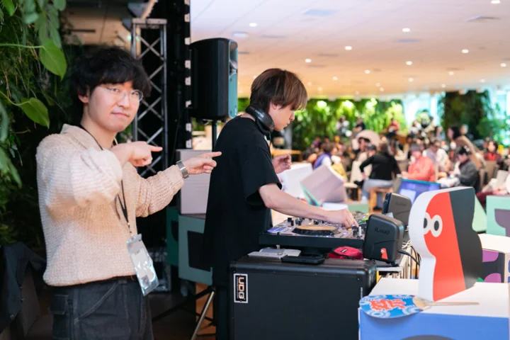 DJブースの機材を囲む二人と、その奥の会場
